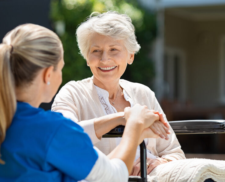Smiling senior patient sitting on wheelchair with nurse supporti